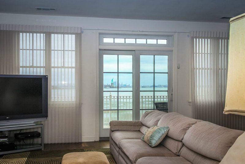 A living room with glass doors overlooking the Statue of Liberty and Hudson River.