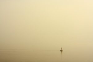 A tiny sailboat that is lost on a vast ocean in a foggy morning.